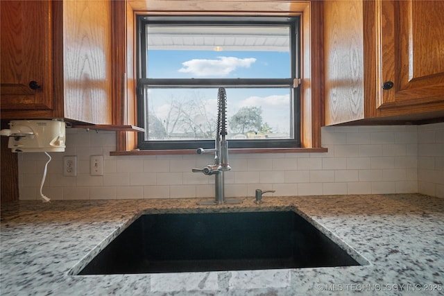 kitchen with tasteful backsplash, light stone counters, brown cabinetry, and a sink