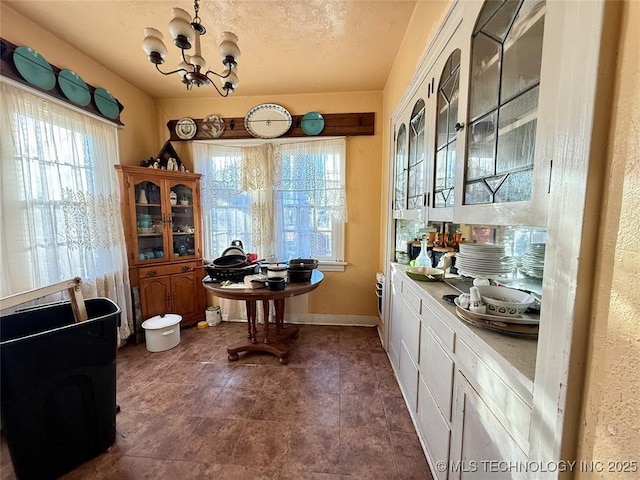 interior space with a notable chandelier, a textured ceiling, baseboards, and a healthy amount of sunlight