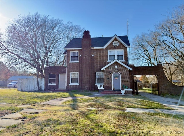 view of front facade with brick siding, a chimney, a front lawn, and fence