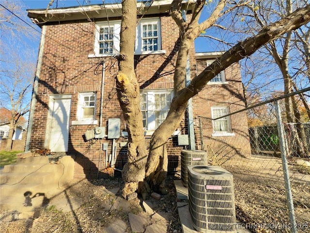 back of property with cooling unit, brick siding, and fence