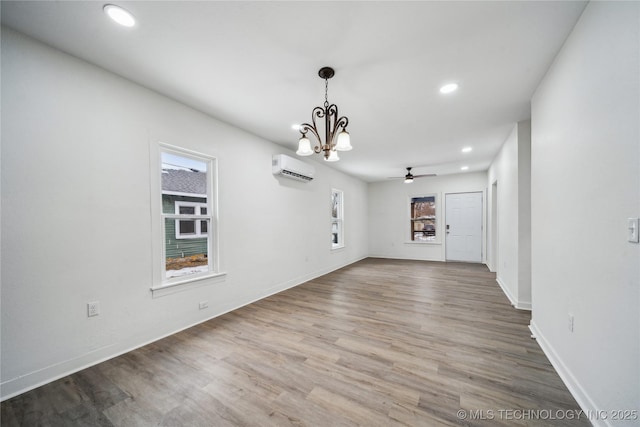 interior space with baseboards, wood finished floors, a wall mounted air conditioner, ceiling fan with notable chandelier, and recessed lighting