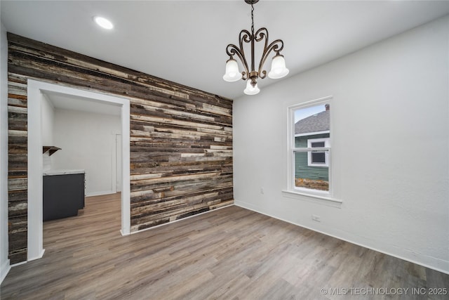 empty room featuring an inviting chandelier, wooden walls, an accent wall, and wood finished floors