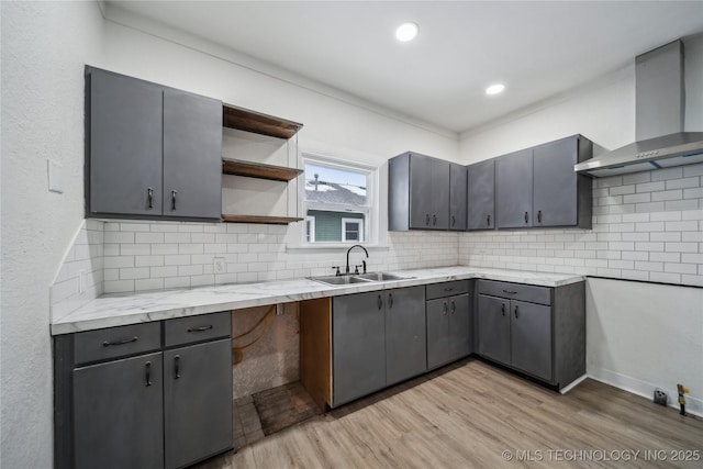 kitchen with gray cabinetry, a sink, wall chimney exhaust hood, and open shelves