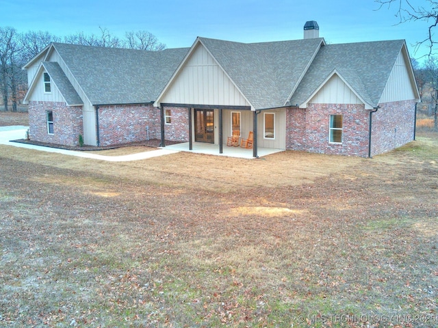 view of front of house with a front yard, roof with shingles, a chimney, and a patio