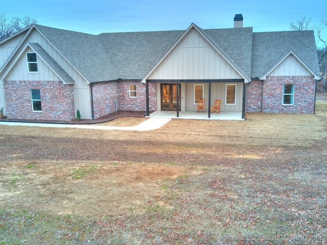 view of front of home featuring roof with shingles, brick siding, a chimney, and board and batten siding