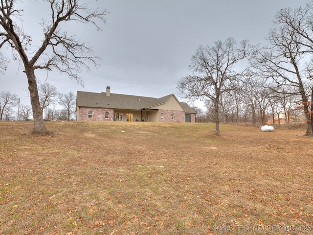 rear view of property featuring brick siding, a lawn, and a chimney