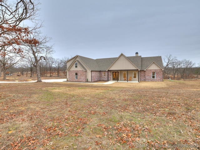 view of front of house featuring brick siding, a chimney, a front lawn, and roof with shingles