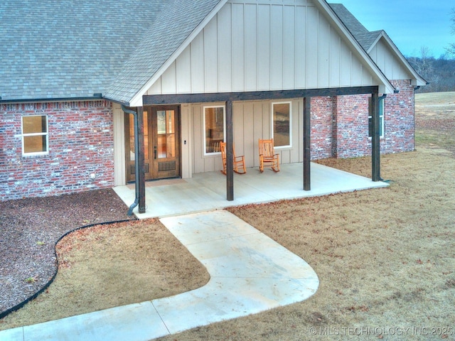 back of house with roof with shingles, a patio, board and batten siding, and brick siding