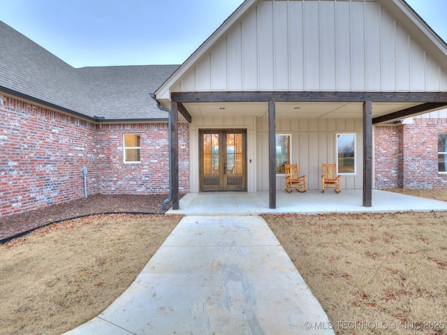 view of exterior entry featuring board and batten siding, brick siding, a lawn, and roof with shingles