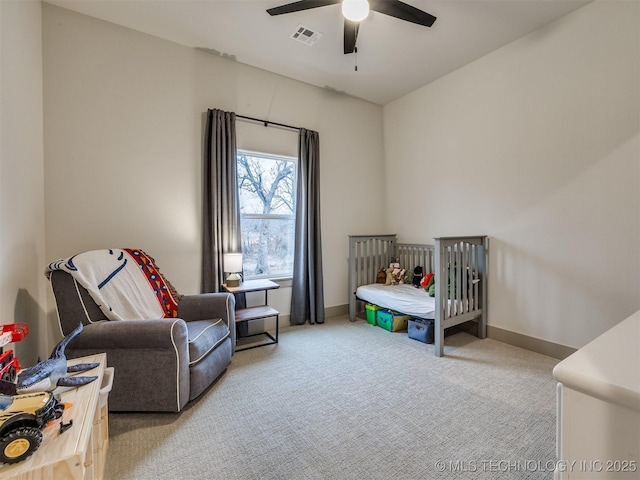 bedroom with a crib, baseboards, visible vents, light colored carpet, and ceiling fan