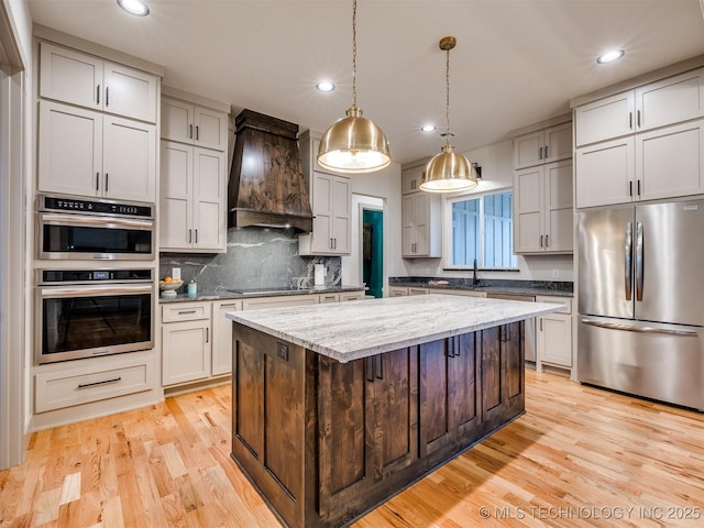 kitchen with a center island, appliances with stainless steel finishes, custom exhaust hood, light stone countertops, and pendant lighting