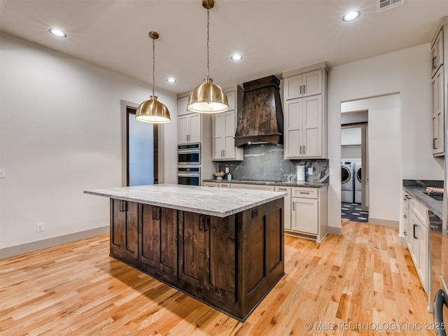 kitchen featuring washer and clothes dryer, custom range hood, a kitchen island, decorative light fixtures, and backsplash