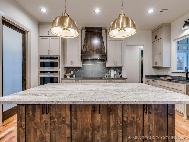 kitchen with decorative light fixtures, stainless steel double oven, black electric cooktop, and custom range hood