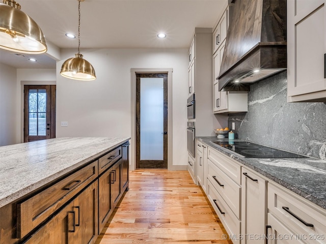 kitchen featuring light stone counters, premium range hood, black electric cooktop, and white cabinets