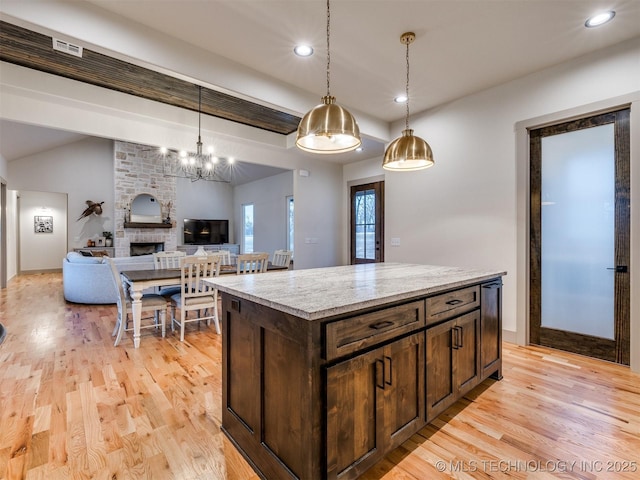 kitchen with dark brown cabinetry, light wood-style flooring, a center island, decorative light fixtures, and a fireplace