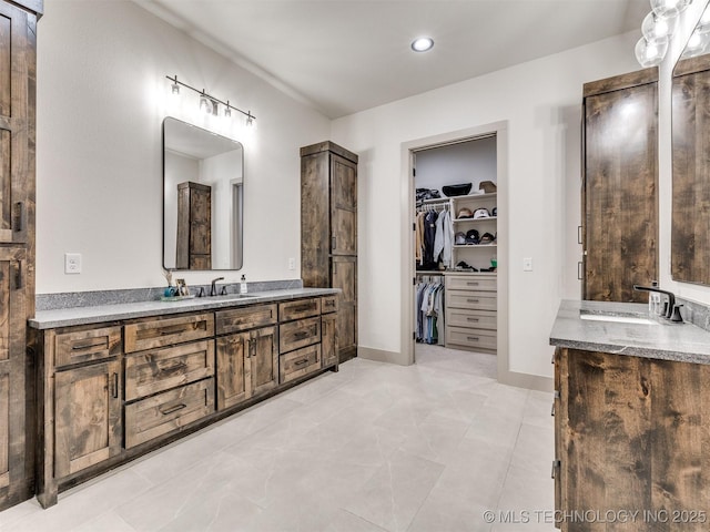 bathroom with a spacious closet, baseboards, two vanities, and a sink