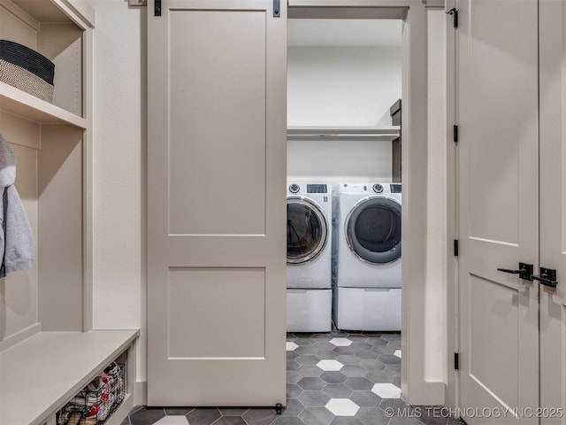 laundry room featuring laundry area, a barn door, washing machine and clothes dryer, and dark tile patterned flooring