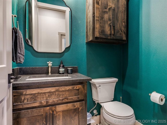 half bath with toilet, a textured wall, and vanity