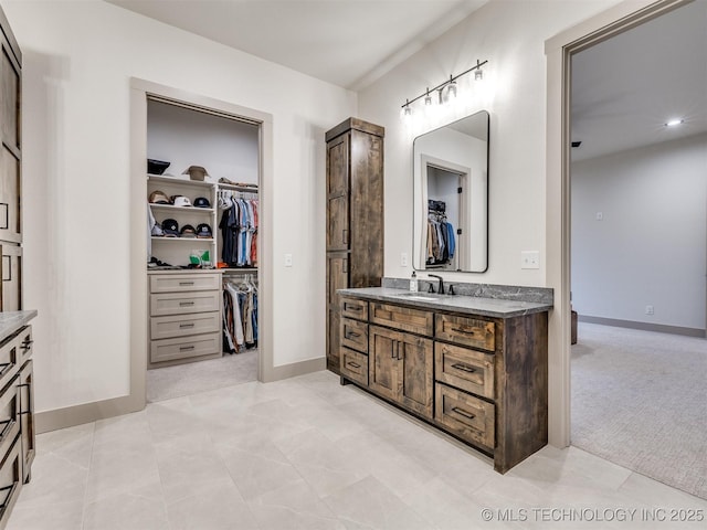 bathroom with a spacious closet, vanity, and baseboards