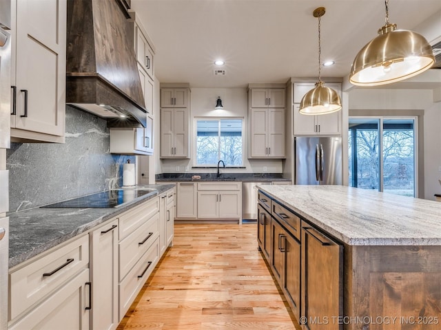 kitchen featuring custom exhaust hood, freestanding refrigerator, white cabinetry, a kitchen island, and black electric cooktop