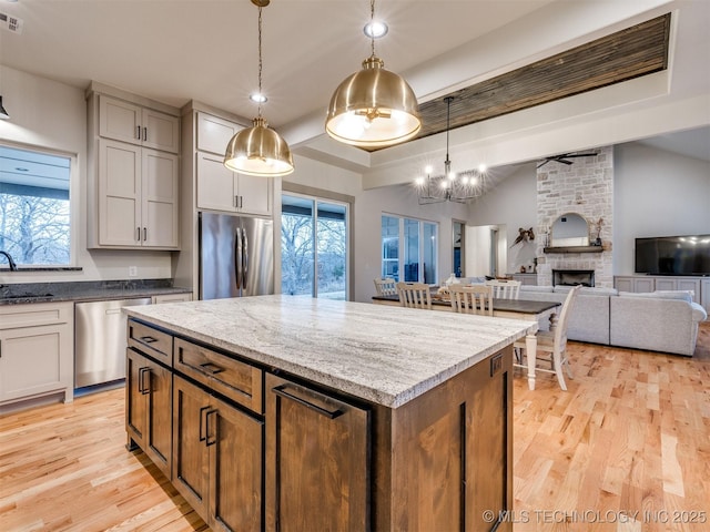 kitchen featuring appliances with stainless steel finishes, open floor plan, decorative light fixtures, a fireplace, and a sink