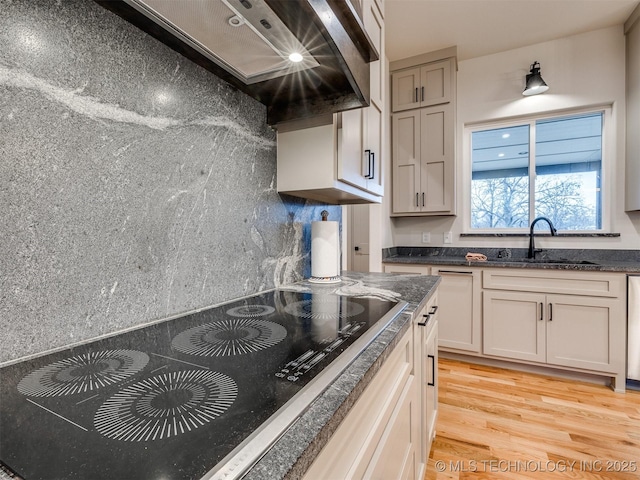 kitchen with light wood-type flooring, premium range hood, black electric cooktop, and a sink