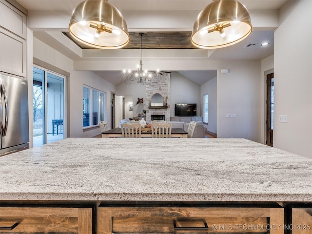 kitchen featuring vaulted ceiling with beams, visible vents, light countertops, a brick fireplace, and stainless steel fridge