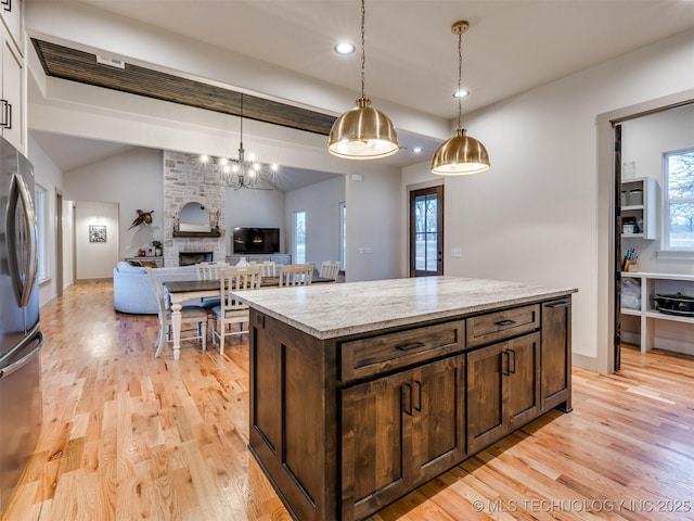 kitchen featuring a fireplace, dark brown cabinets, light wood-type flooring, freestanding refrigerator, and pendant lighting