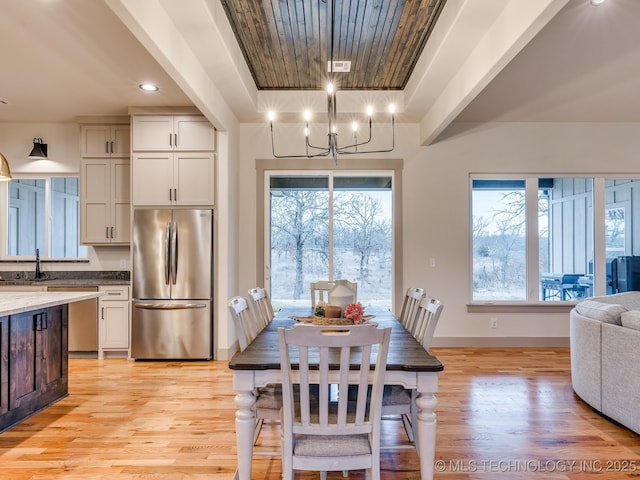 dining area featuring baseboards, a tray ceiling, an inviting chandelier, and light wood-style floors