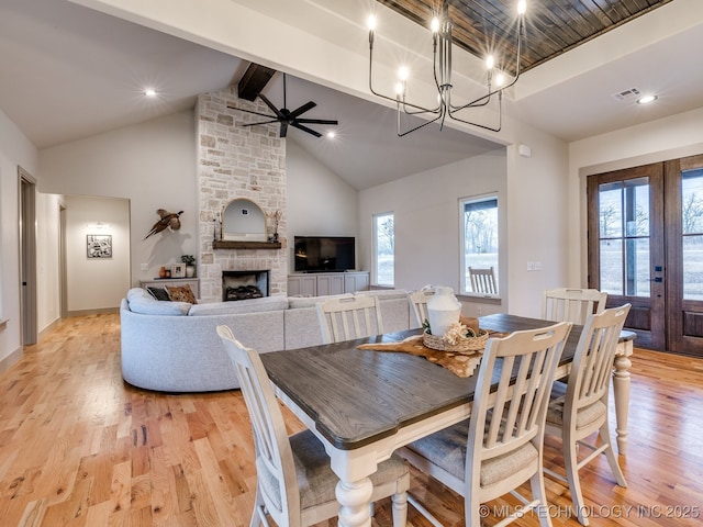 dining room featuring high vaulted ceiling, light wood-style flooring, ceiling fan with notable chandelier, a fireplace, and beamed ceiling