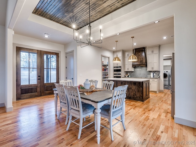 dining area with light wood-style flooring, baseboards, french doors, washer / clothes dryer, and a raised ceiling