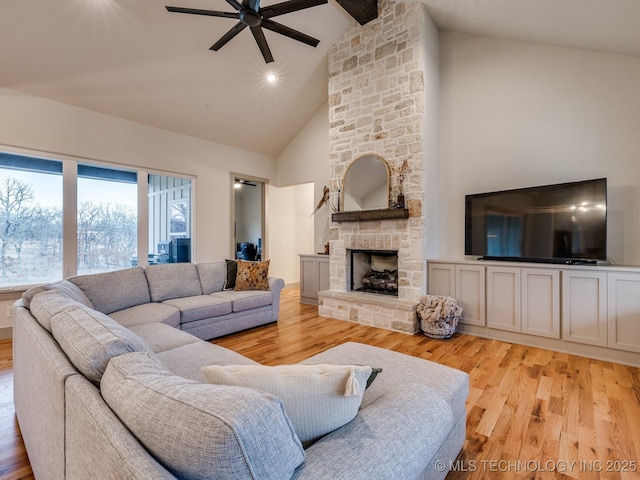 living area featuring light wood finished floors, ceiling fan, beam ceiling, and a stone fireplace