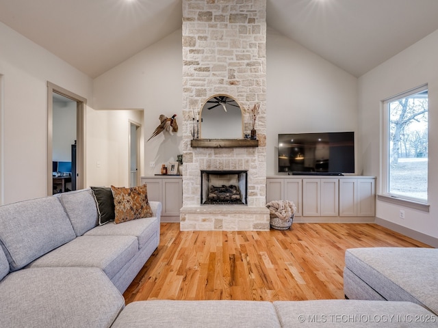 living room with light wood-style floors, high vaulted ceiling, a stone fireplace, and baseboards