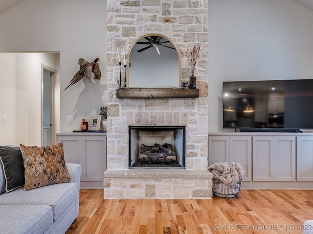 living area with vaulted ceiling, a stone fireplace, and light wood-style floors