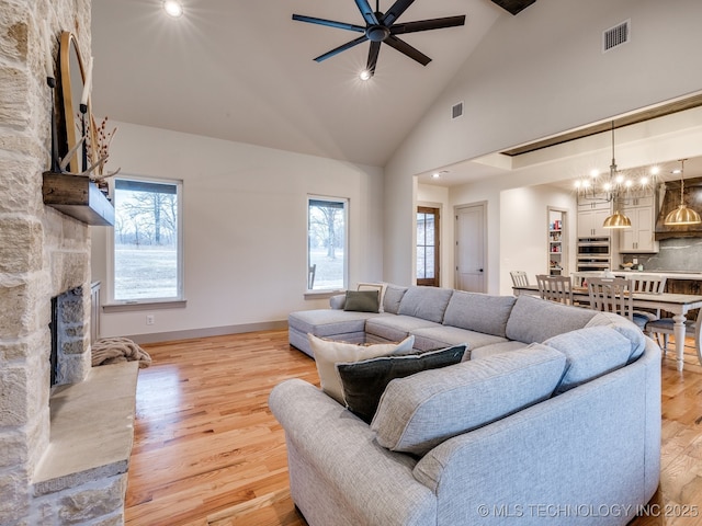 living room featuring visible vents, a ceiling fan, light wood-type flooring, a fireplace, and high vaulted ceiling