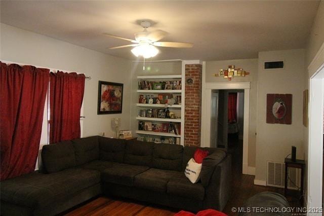 living room featuring built in shelves, visible vents, ceiling fan, and dark wood-type flooring