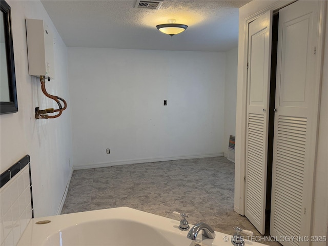 bathroom featuring baseboards, water heater, visible vents, and a textured ceiling