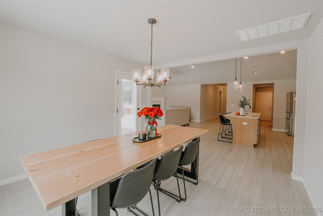 dining room featuring light wood finished floors, an inviting chandelier, visible vents, and baseboards