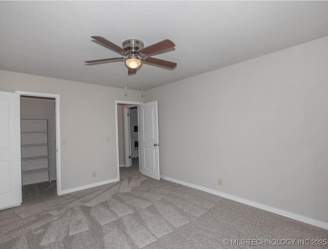 unfurnished bedroom featuring light carpet, ceiling fan, a spacious closet, and baseboards