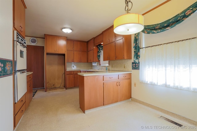 kitchen featuring white oven, light countertops, a peninsula, brown cabinets, and visible vents