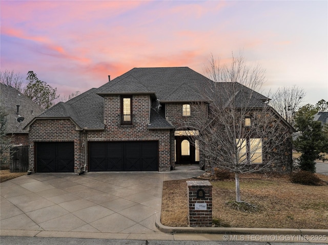 french country style house featuring a garage, roof with shingles, concrete driveway, and brick siding