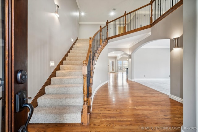 foyer entrance featuring arched walkways, a towering ceiling, ornamental molding, wood finished floors, and baseboards