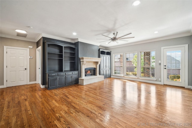 unfurnished living room featuring wood finished floors, a ceiling fan, visible vents, a glass covered fireplace, and crown molding