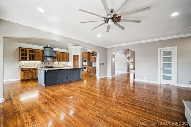 unfurnished living room with arched walkways, wood finished floors, and a ceiling fan