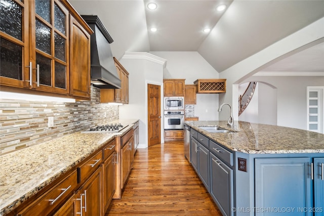 kitchen with appliances with stainless steel finishes, glass insert cabinets, a center island with sink, and a sink