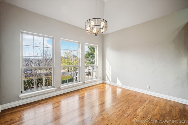 unfurnished dining area with a notable chandelier, baseboards, and wood finished floors