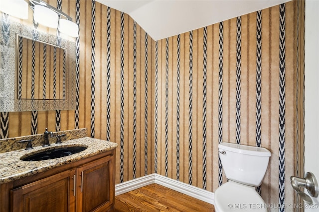 half bathroom featuring vaulted ceiling, vanity, toilet, and wood finished floors