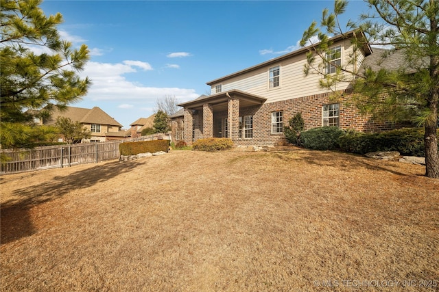 back of house with a yard, brick siding, and fence