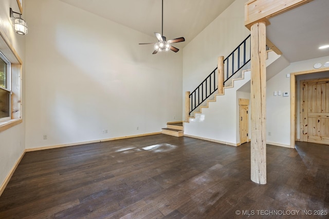 unfurnished living room with a towering ceiling, baseboards, stairway, and dark wood-type flooring