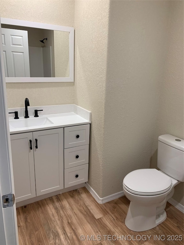 bathroom with baseboards, a textured wall, toilet, wood finished floors, and vanity